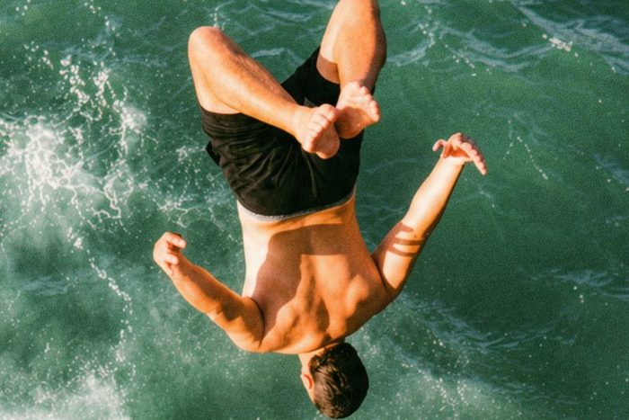 A swimmer flipping backwards into deep green sea