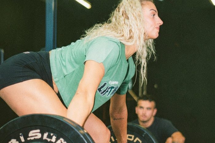A woman setting up a heavy barbell deadlift while a coach watches