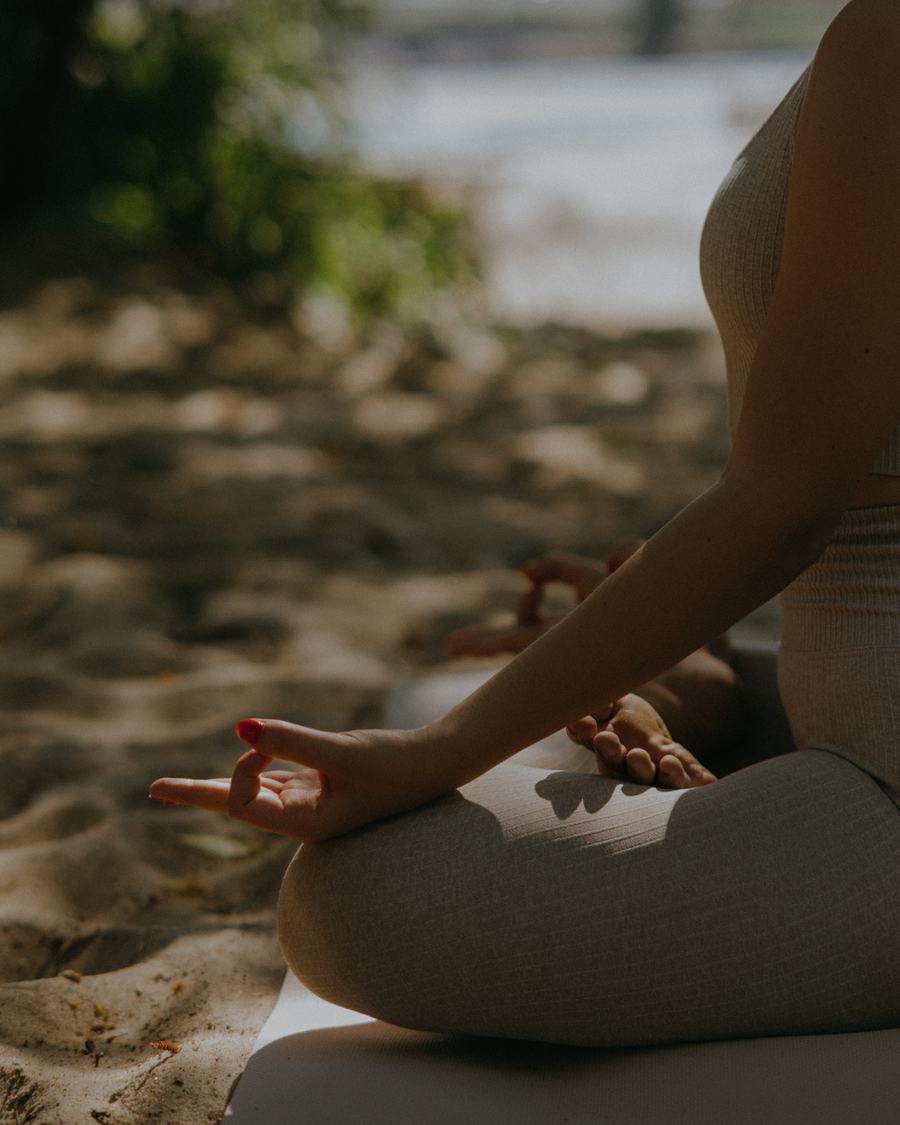 Woman meditating cross-legged on the sand in dappled light