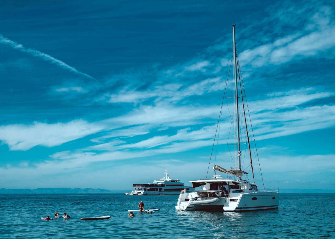 Catamaran at anchor on flat blue water, with swimmers and paddle boards alongside