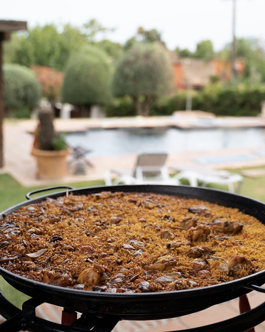 A large pan of paella on the terrace, with the villa pool and garden behind
