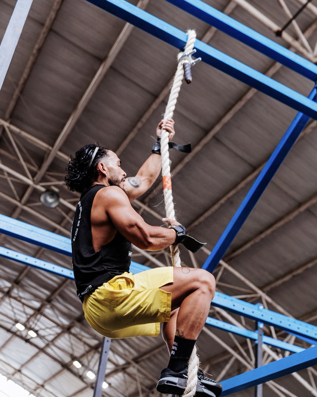 Athlete climbing a rope under the steel roof of a big gym