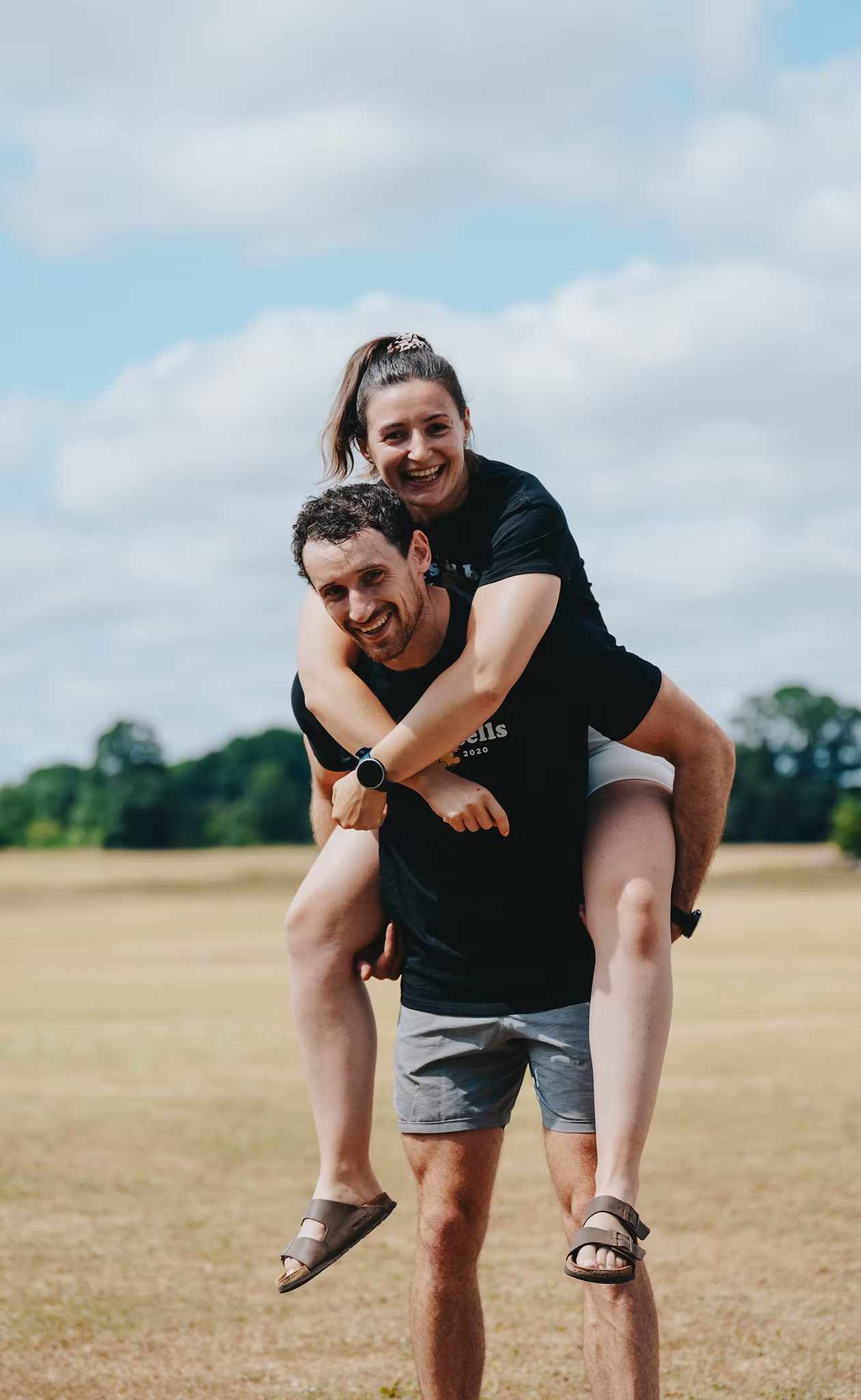 A woman on a man’s back in a sunny field, both laughing